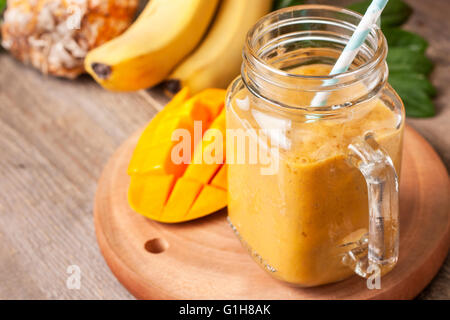 Smoothie mit tropischen Früchten: Mango, Banane, Ananas im Weckglas Mason auf dem alten hölzernen Hintergrund Stockfoto