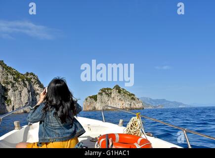 Eine Frau in einem gelben Kleid und Jacke Jean Fotografieren an der Vorderseite ein Boot auf eine Tour rund um Capri Insel Italien Stockfoto