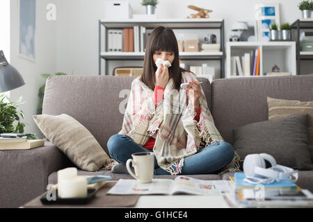 Kranke Frau mit Erkältung und Grippe, ruht sie auf dem Sofa zu Hause und Messung der Körpertemperatur mit einem thermometer Stockfoto