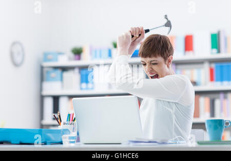 Betonte Frau schreien und zerstören ihren Laptop mit einem Hammer, Computerprobleme und Konzept überarbeiten Stockfoto