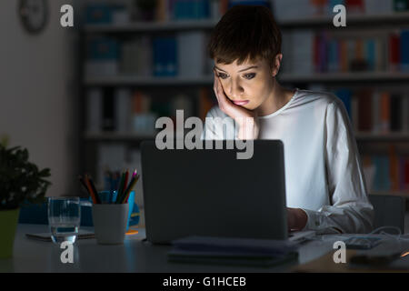 Junge attraktive Frau am Schreibtisch sitzen und arbeiten mit einem Laptop spät in die Nacht Stockfoto