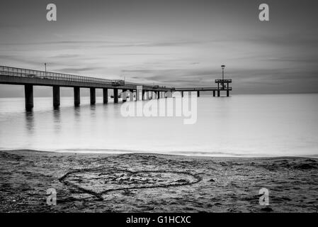 Sonnenaufgang über eine Seebrücke. Herzen in den Sand gezeichnet. Stockfoto