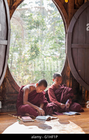 Zwei junge buddhistische Mönche in einem roten buddhistischen Kleid vor ein offenes Fenster, das Studium der Heiligen Bücher in einem buddhistischen Tempel. Stockfoto