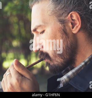 Bärtige asiatischer Mann zündet eine Zigarre, Outdoor-Vierkantprofil Portrait mit selektiven Fokus Stockfoto