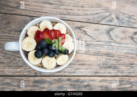 Acai Schüssel mit frischem Obst, Erdbeere, Heidelbeere, Banane und Pfefferminze Blätter an der Spitze auf dem Holztisch. Stockfoto