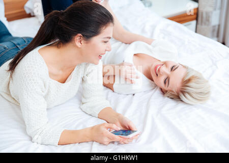 Zwei glückliche Mädchen auf dem Bett liegend und Klatsch zu Hause Stockfoto