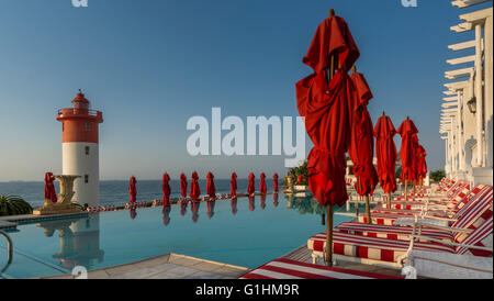 Sonnenliegen und rote Sonnenschirme warten auf Gäste am Pool eines Luxus-Hotels in Durban, KwaZulu Natal, Südafrika Stockfoto