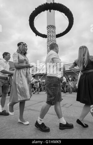 Frauen und Männer in lokalen Kostümen tanzen einen traditionellen bayerischen Volkstanz rund um den Maibaum mit Bändern Stockfoto