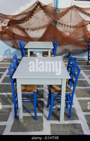 Blaue Stühle & Cyan leer Fisch Restauranttische auf weiß getünchten karierten Boden & Angeln Netze Hintergrund. Myrina Lemnos Griechenland. Stockfoto