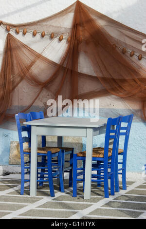 Satz von Cyan leer Taverne und blauen Stühlen auf karierten Boden & hängende Fischerei Netze Wanddekoration. Myrina, Limnos, Griechenland. Stockfoto