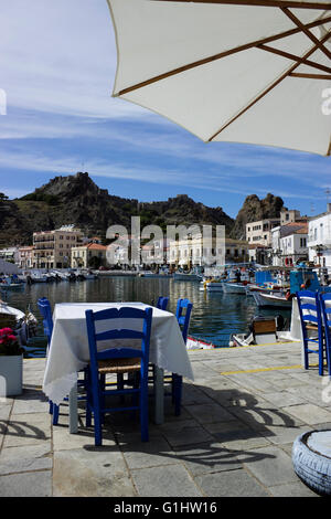 Leere griechische Taverne Tisch mit blauen Stühlen und geöffneten weißen Sonnenschirm mit Blick auf das Schloss und der Architektur. Limnos Stockfoto