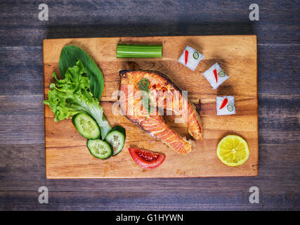 Gegrillter Lachs mit Gemüse und Reis auf Holzplatte und rustikalen Tisch. Ansicht von oben Stockfoto