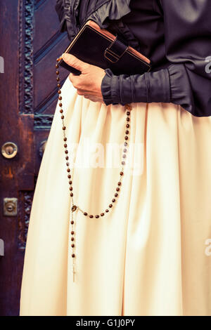 Detail der Womans Hand mit Bibel und Rosenkranz Perlen, Ende des 19. Jahrhunderts Kleid, aus Holz geschnitzte Tür. Stockfoto