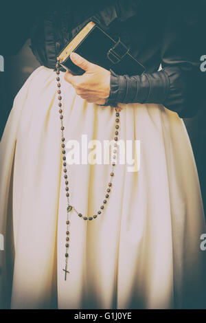 Detail der Womans Hand, die Bibel und Rosenkranz Perlen, Ende des 19. Jahrhunderts Kleid. Stockfoto