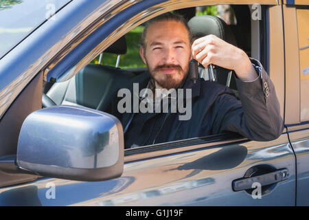 Lächelnder asiatischen Mann mit Schlüssel als treibende Kraft der modernen japanischen Suv, Outdoor-Porträt in offenen Autofenster Stockfoto