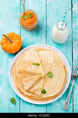 Dünne Crêpes oder Pfannkuchen mit frischen Kürbis Confiture, Marmelade und Flasche Milch auf einer rustikalen hölzernen Hintergrund-Draufsicht Stockfoto