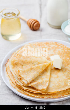 Dünne Crêpes oder Pfannkuchen mit Butter, Honig und Sauerrahm auf einem rustikalen Textil-Hintergrund Stockfoto