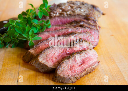 Gegrillte Flacheisen Steak geschnitten auf einem Brett aus Holz schnitzen, garniert mit Kräutern und fotografiert in natürlichem Licht Stockfoto