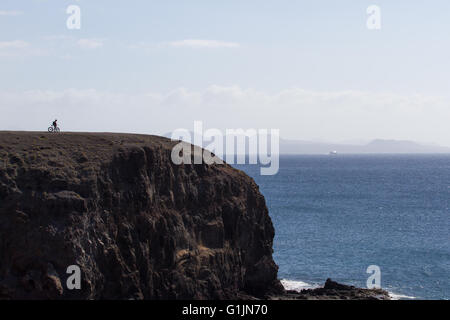 Malerischen Felsen über dem Meer. Radfahrer auf einem Hintergrund von Himmel und Stein, Papagayo Strand Lanzarote Stockfoto