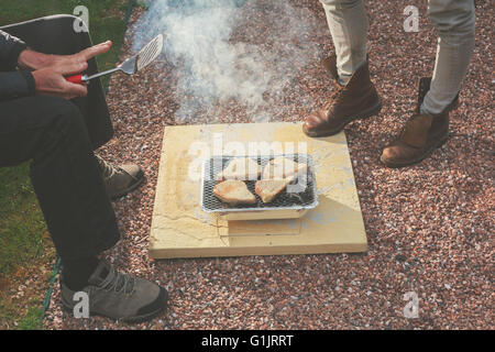 Zwei Personen stehen herum ein Einweg-Grill Stockfoto