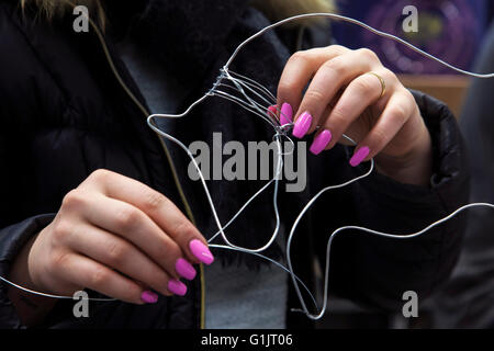 Hände mit rosa Nägel verbiegen einen Draht Stockfoto