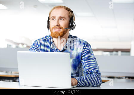 Glücklichen hübscher junger Mann mit Kopfhörer und Laptop im Büro Stockfoto
