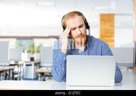 Traurig deprimiert junger Mann mit Kopfhörer und Laptop leiden unter Kopfschmerzen am Arbeitsplatz Stockfoto