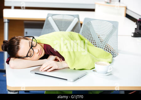Geschwächt, müde junge Geschäftsfrau, bedeckt mit Decke schlafen am Arbeitsplatz Stockfoto