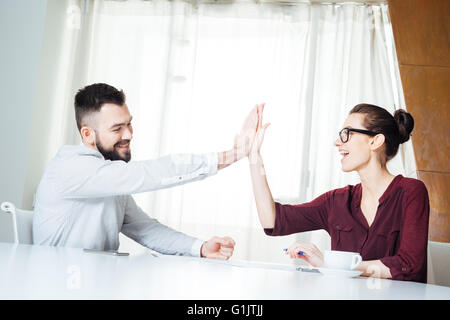 Zwei glückliche erfolgreiche junge Unternehmer sitzen und geben hohe fünf über die Tagung Stockfoto