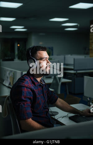 Ernsthafte bärtiger junger Geschäftsmann Kopfhörer Überstunden im Büro Stockfoto