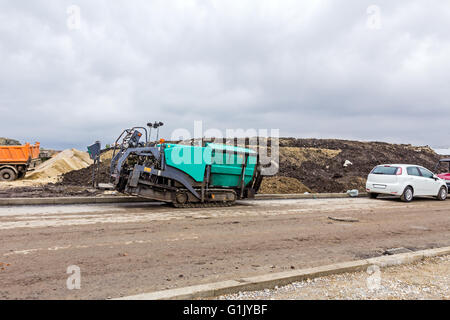 Seitliche Sicht auf Asphalt Verlegung Maschine auf Baustelle. Heißer Asphalt breitet sich mit fertiger Maschine auf vorbereitetem Boden. Stockfoto