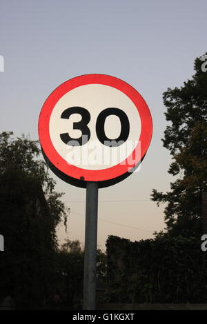 Tempolimit Schild 30 30 km/h Meilen pro Stunde beleuchtet gegen Abend schlau und Bäume. Stockfoto