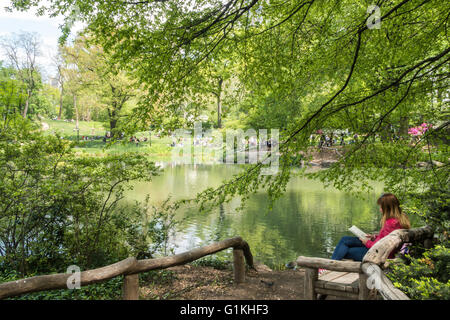 Frau liest ein Buch über die Holzbank, Teich, Central Park, New York, USA Stockfoto