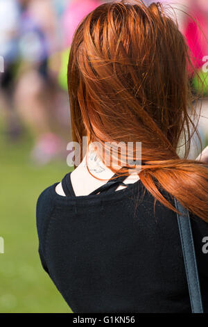 Junge Frau mit langen Ingwer Haar mit Wind Haar, fliegenden Vogel Tattoo bei Veranstaltung am Poole zu offenbaren Stockfoto