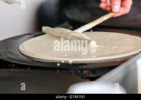 Ein Mann verbreitet Teig auf eine Herdplatte, Crêpes zu machen. Stockfoto