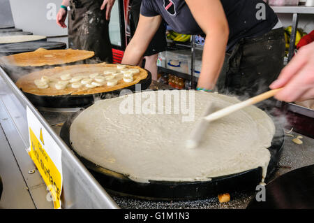 Ein Mann verbreitet Teig auf eine Herdplatte, Crêpes zu machen. Stockfoto