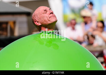 Ein Kinder Darsteller schiebt seinen Kopf aus einem großen grünen aufblasbarer Ballon. Stockfoto