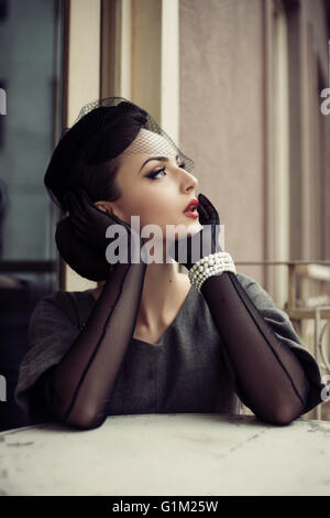 Schöne Retro-Frau am Tisch sitzen und nach oben schauen Stockfoto