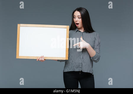 Junge Geschäftsfrau, die leere Kammer über grauen Hintergrund zu halten Stockfoto