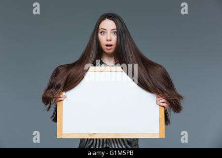 Schöne Frau mit langen Haaren, die leere Kammer über grauen Hintergrund zu halten Stockfoto