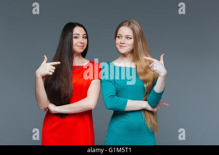Zwei glückliche Freundinnen Schuldzuweisungen an einander über grauer Hintergrund Stockfoto