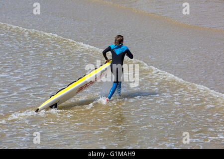 RNLI Rettungsschwimmer, der Rettungsschwimmer mit einem Surfbrett aus dem Meer am Bournemouth Beach im Rahmen einer Trainingsübung im Mai in Bournemouth, Dorset, Großbritannien, trägt Stockfoto