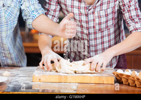 Hände des jungen Paares Mehl und kneten den Teig auf die Küche Stockfoto