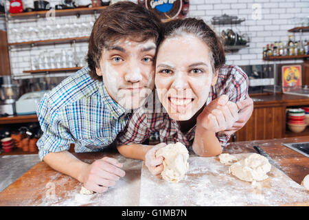 Junges Paar mit Mehl auf Gesichtern lustige Grimassen und Kneten von Teig Stockfoto