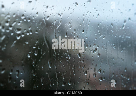 Regentropfen, die an einem nassen, regnerischen Tag durch ein Fenster laufen, mit einer verschwommenen Stadtlandschaft dahinter. Stockfoto