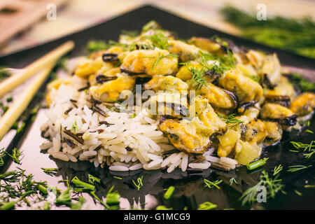 Miesmuscheln mit Reis in cremiger Sauce in eine schwarze Glasplatte Stockfoto