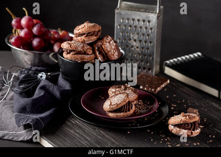 Italienische Maroni Cookies auf dem Teller und Schale mit Trauben, Tuch, Notebook auf dunklen alten hölzernen Hintergrund Stockfoto