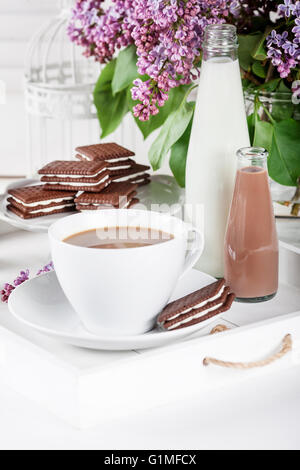Tasse Kaffee und einige Flaschen Milch und Schokolade Miklshakes auf einem weißen Tablett mit lila Blumen auf weißen Fensterläden Hintergrund