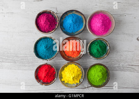 Farbenfrohe Holi-Pulver in Tassen auf weißem rustikalen Holztisch. Draufsicht mit Textfreiraum. Stockfoto