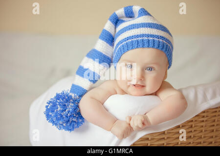 Entzückende lächelndes Babymädchen in blauer Strickmütze liegt im Korb Stockfoto